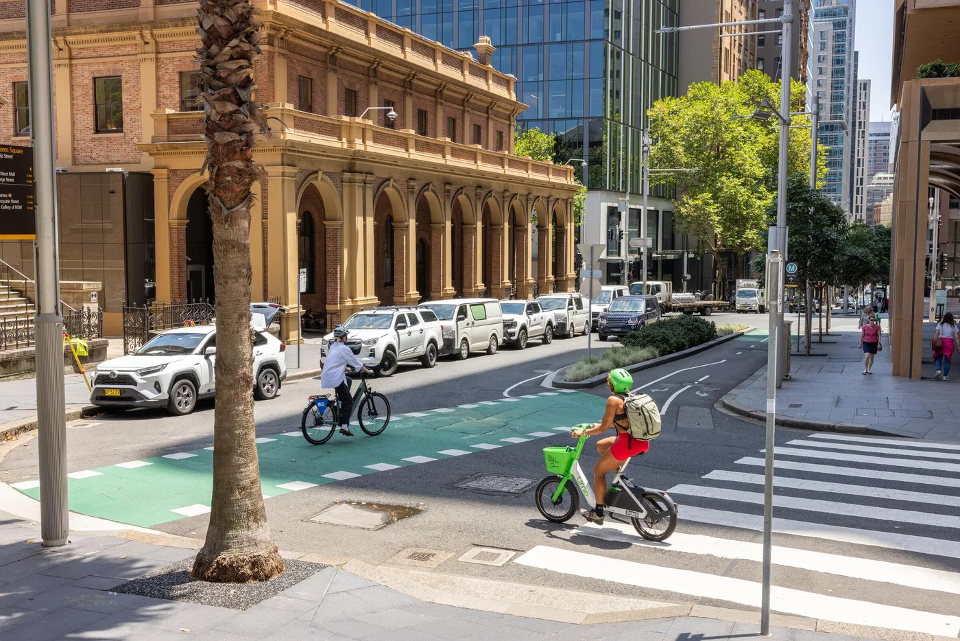 People cycling along a leafy Sydney street, beside historic sandstone buildings.